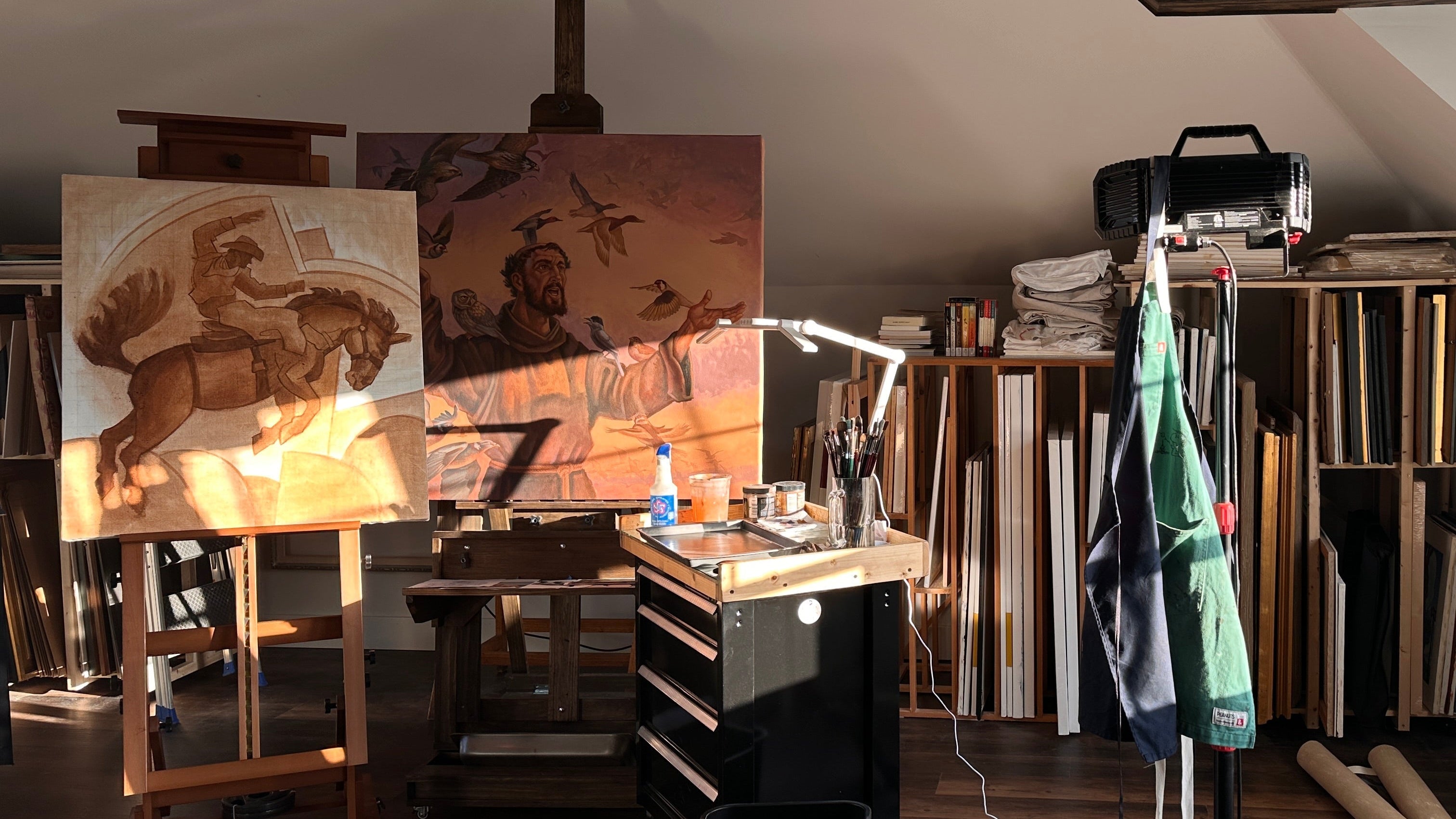 Art studio with easels, paintings, and art supplies on a wooden floor.